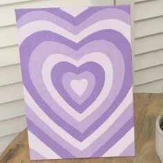 a purple and white heart painting sitting on top of a table next to a potted plant