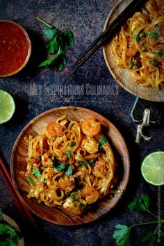 two bowls filled with shrimp and noodles next to chopsticks, lime wedges and cilantro