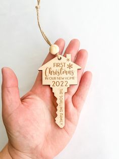 a hand holding a wooden key shaped ornament that says first christmas in your new home