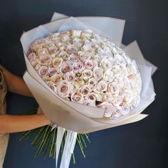 a woman holding a large bouquet of white and pink roses in front of a blue wall