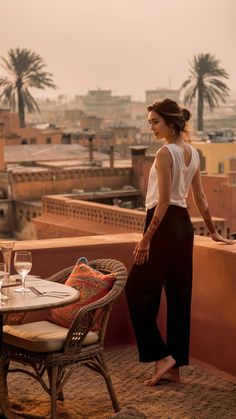 a woman standing on top of a roof next to a chair and table with wine glasses