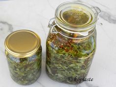 two glass jars filled with different types of herbs on a marble counter top next to each other