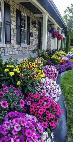 many different colored flowers line the side of a house's front yard, along with another flower bed