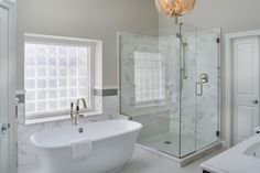 a white bath tub sitting next to a walk in shower and a sink under a light fixture