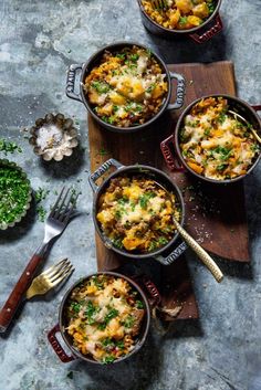 three pans filled with food on top of a wooden cutting board next to silverware