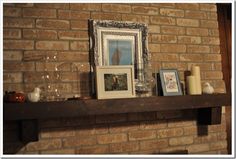 a mantle with pictures and candles on it in front of a brick wall that has a fireplace