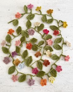 crocheted flowers arranged in a circle on a white surface with green stems and leaves