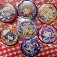 six buttons with anime characters on them sitting on a tableclothed surface in front of a red and white checkered cloth