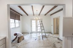 a man is painting the ceiling in an empty room with white walls and wood beams