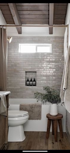 a white toilet sitting next to a bath tub in a bathroom on top of a hard wood floor