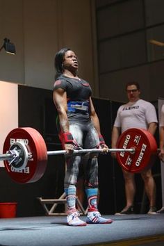 a woman holding a barbell on top of a stage with other people standing around