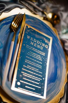 a blue plate topped with a menu on top of a wooden table next to a fork and knife