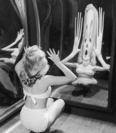 a woman sitting on the floor in front of a mirror with her hands up and arms outstretched