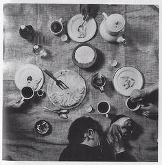 black and white photograph of people sitting at a table with plates, cups and utensils