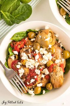 two white bowls filled with vegetables and meat on top of a table next to silverware