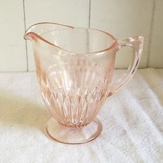 a pink glass pitcher sitting on top of a white cloth covered table next to a wall