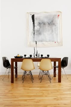 a dining room table with four chairs and a painting on the wall above it in an empty room