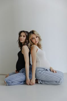 two young women sitting on the floor posing for a photo in front of a white wall