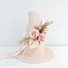 a three tiered cake with pink flowers and feathers on the top is sitting on a white table