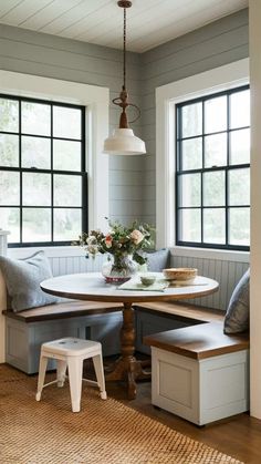 a kitchen table and bench in front of two windows