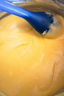 a blue spoon is in a bowl filled with yellow liquid and cheesecake batter on the side