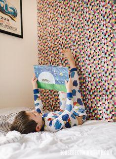 a little boy laying on top of a bed holding an open book in his hands