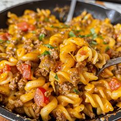 a skillet filled with pasta and meat on top of a wooden table next to a fork