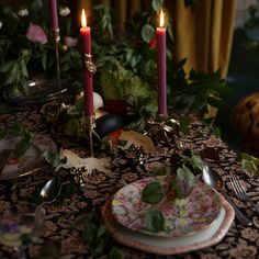 a table topped with plates and candles next to flowers on top of a table cloth