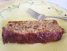 a piece of meatloaf sitting on top of a yellow plate next to a fork