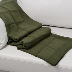 a green blanket is folded on top of a white couch