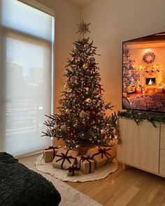 a decorated christmas tree in a living room next to a window with the tv on