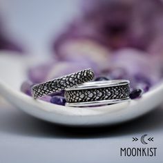 two silver rings sitting on top of a white plate with purple flowers in the background