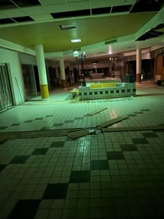 an empty swimming pool in a large building with tiled flooring and green lights on the ceiling