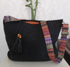 a black crocheted bag sitting on top of a table next to a flower