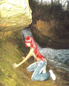 a woman with red hair sitting on the ground next to a waterfall