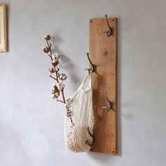 a white bag hanging on a wall next to a hook with hooks and flowers in it