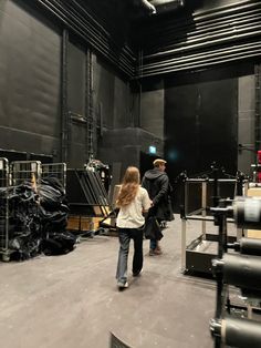 two people are walking around in a large room with black walls and metal pipes on the ceiling