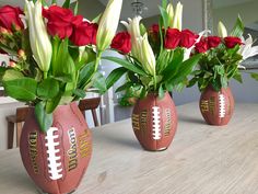 three football vases with flowers in them on a table