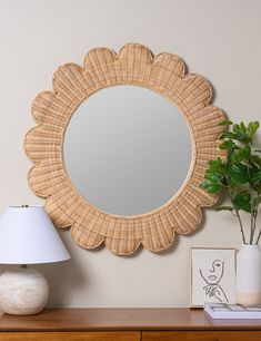 a round mirror sitting on top of a wooden dresser next to a lamp and potted plant