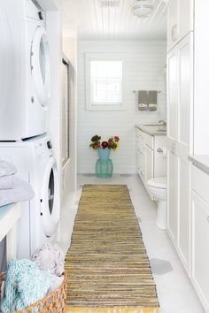 a washer and dryer in a white bathroom with flowers on the rug next to it