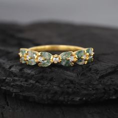 a gold ring with green and white stones sitting on top of a piece of wood