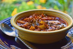 a yellow bowl filled with chili on top of a blue plate next to a spoon