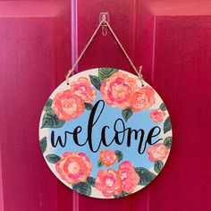 a welcome sign hanging on a red door with pink flowers and the word welcome painted on it