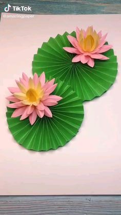 two paper lotus flowers sitting on top of green leaves