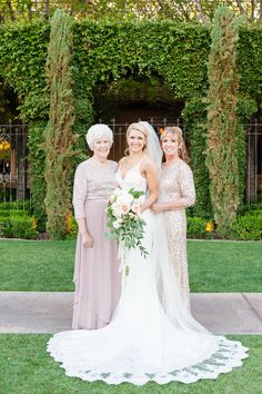 three women standing next to each other in front of some bushes