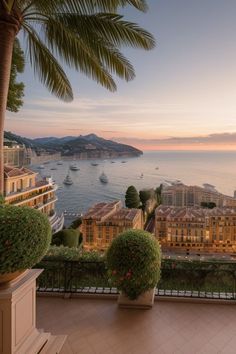 a balcony with potted plants overlooking the ocean and yachts in the bay at sunset