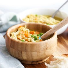 a wooden bowl filled with pasta and peas next to another bowl full of bread on a cutting board