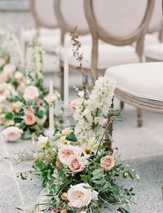 rows of white and pink flowers on the ground in front of chairs with candlesticks