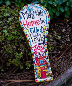 a painted wooden spoon sitting on top of a pile of dirt next to bushes and plants