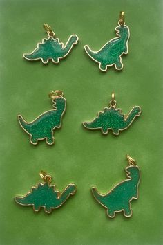 four green dinosaur charms sitting on top of a green surface with gold trimmings